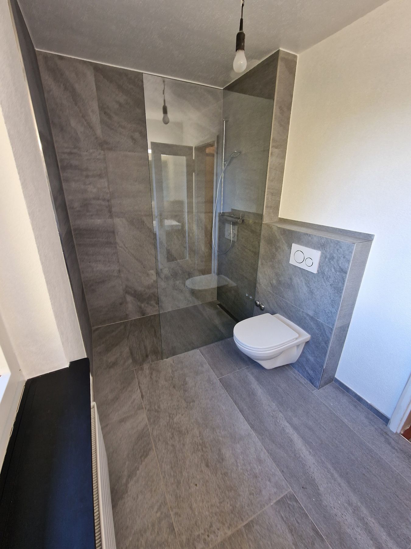Bodenebene Dusche mit grossformatigen Fliesen, Glasabtrennung und WC