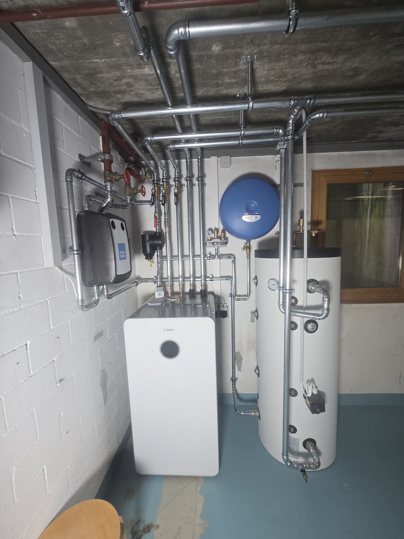 Heizungsraum mit Speicher, Wärmepumpen-Inneneinheit und Rohrleitungen